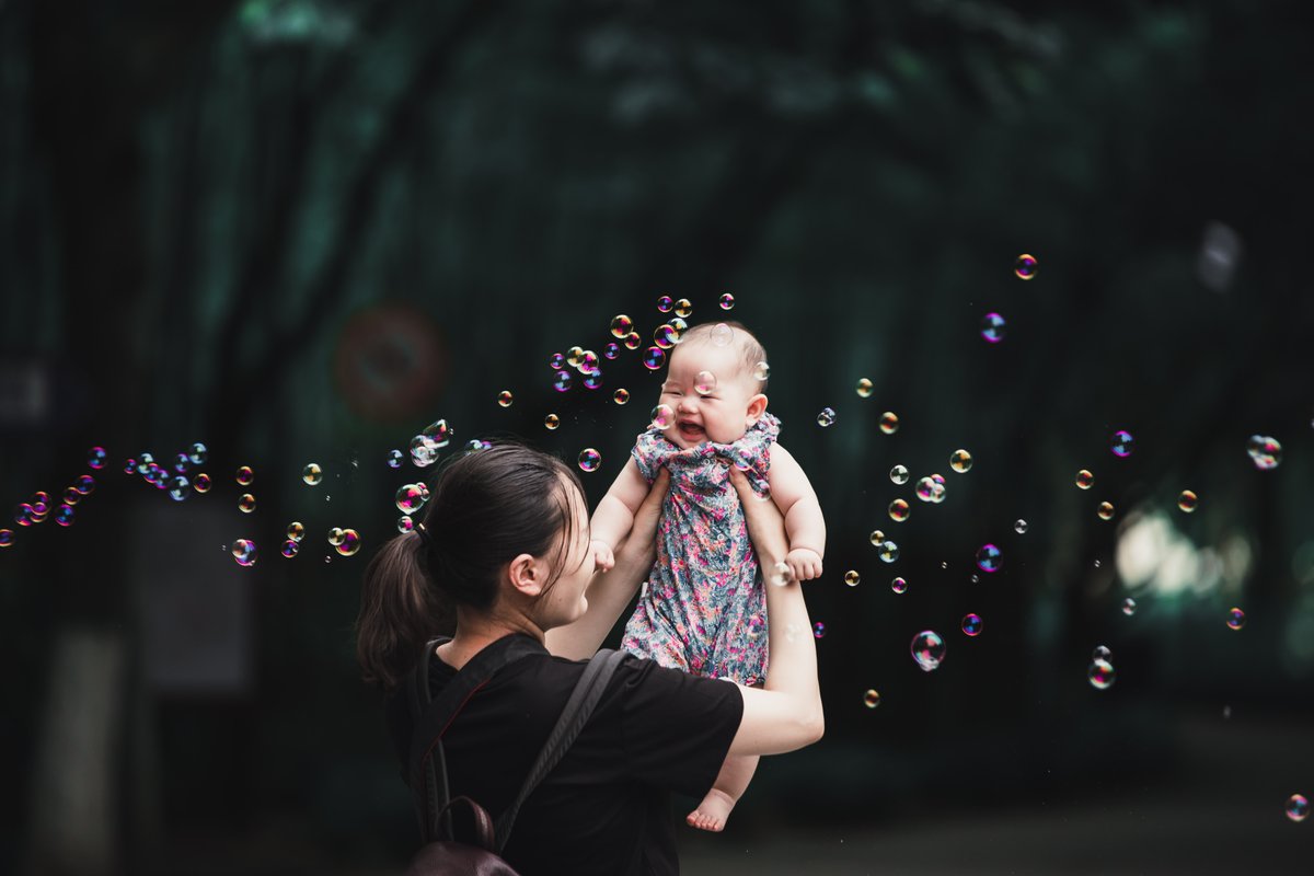 Baby in mothers arms smiling at bubbles