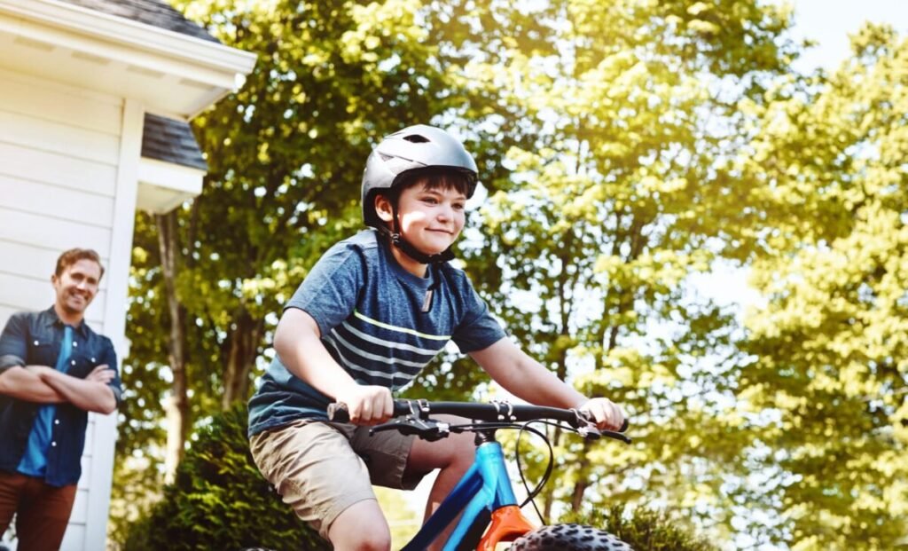 Boy learning how to ride a bike wearing helmet with dad smiling at him with pride 