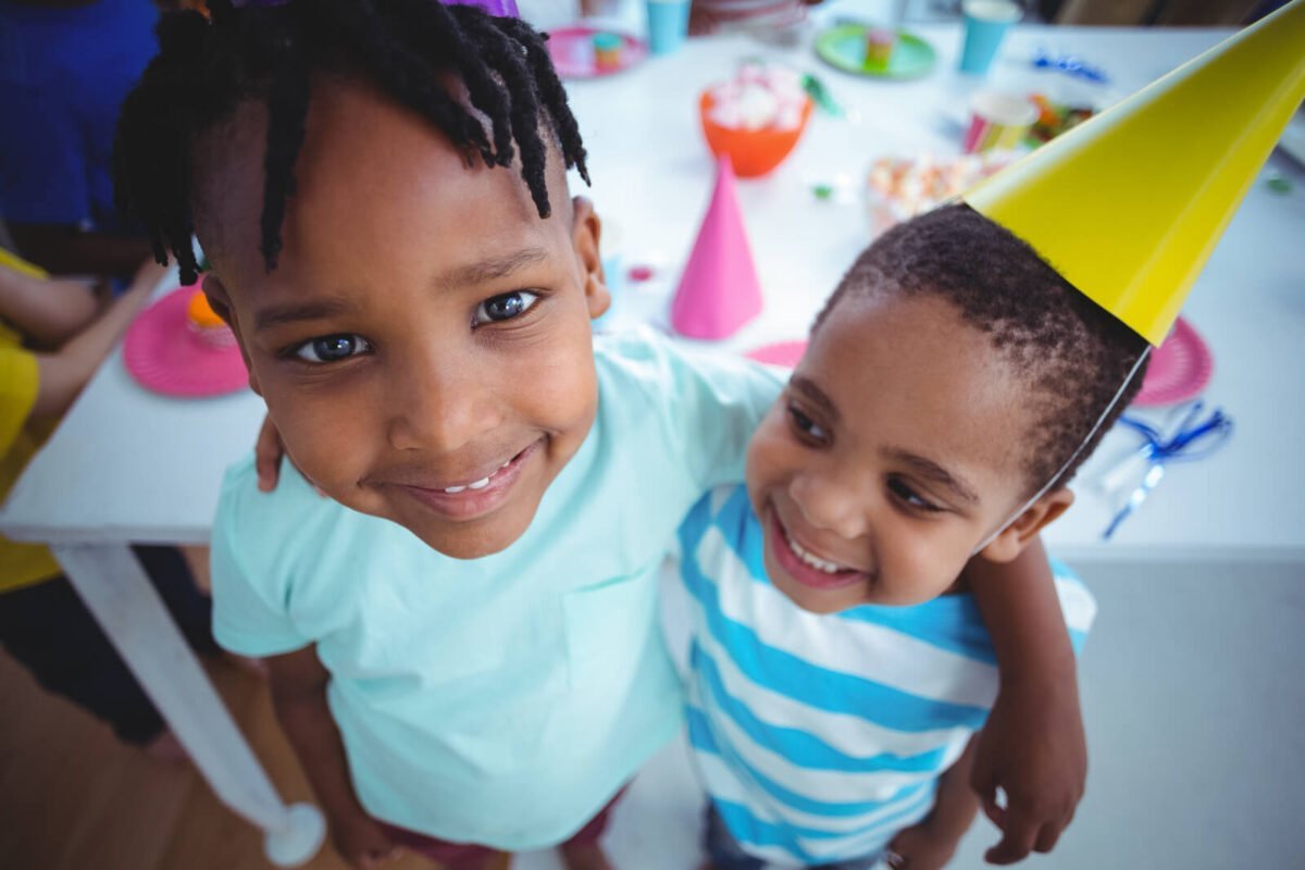 Two young brothers smiling at the camera with their arms around each other celebrating at a birthday party