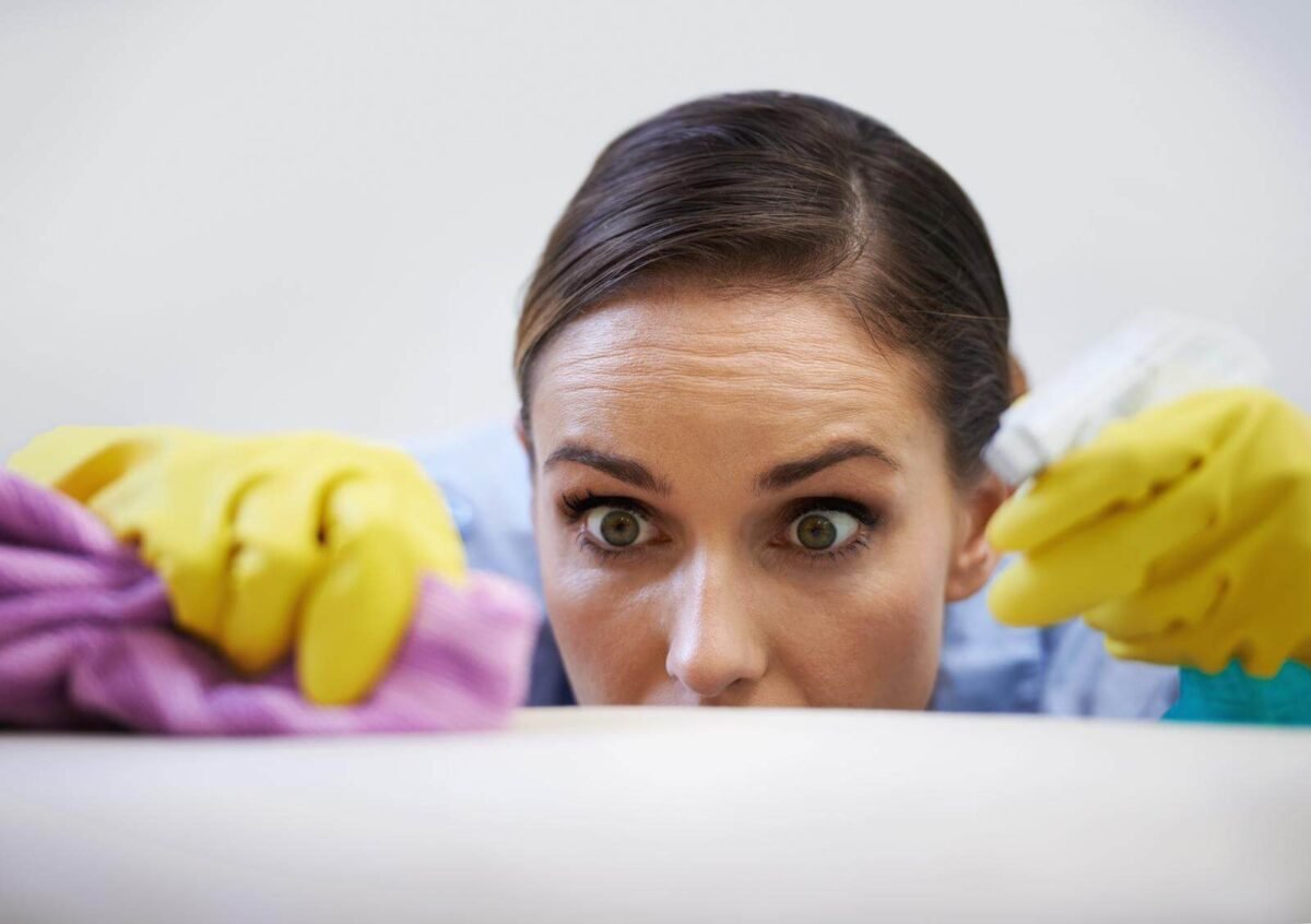 Young woman obsessively cleaning her house wearing yellow gloves and holding cleaning spray
