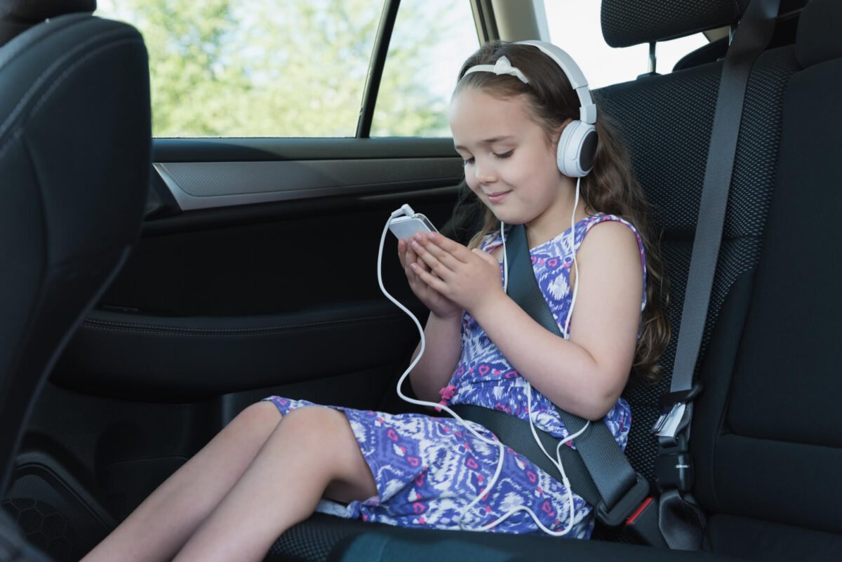 Young girl with headphones listening to music in car on mobile phone
