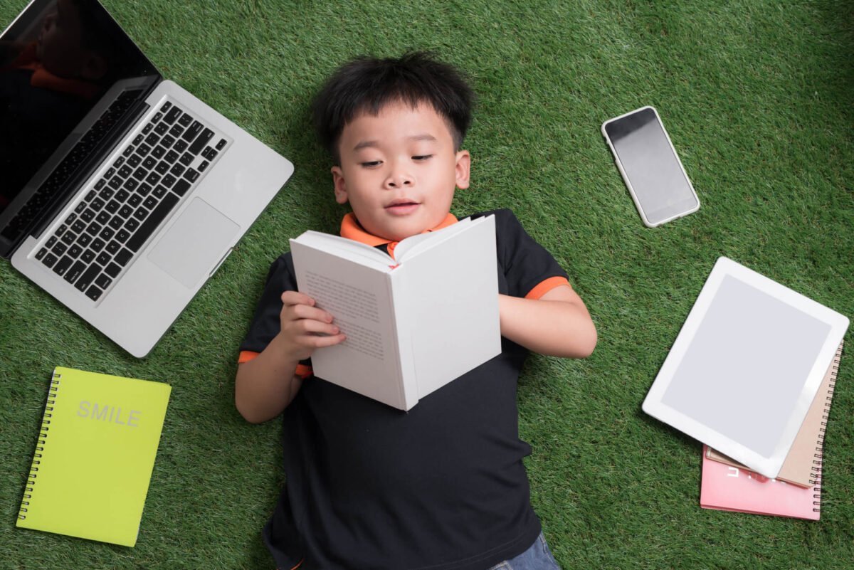 Young child reading a book surrounded by technology