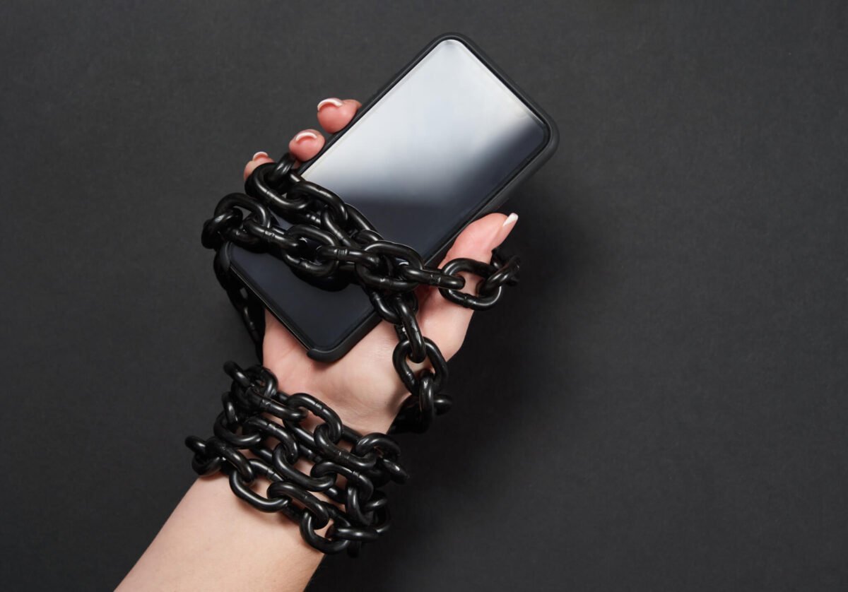 Iron chain that ties together hand and smartphone in concept of social media and internet addiction an black background