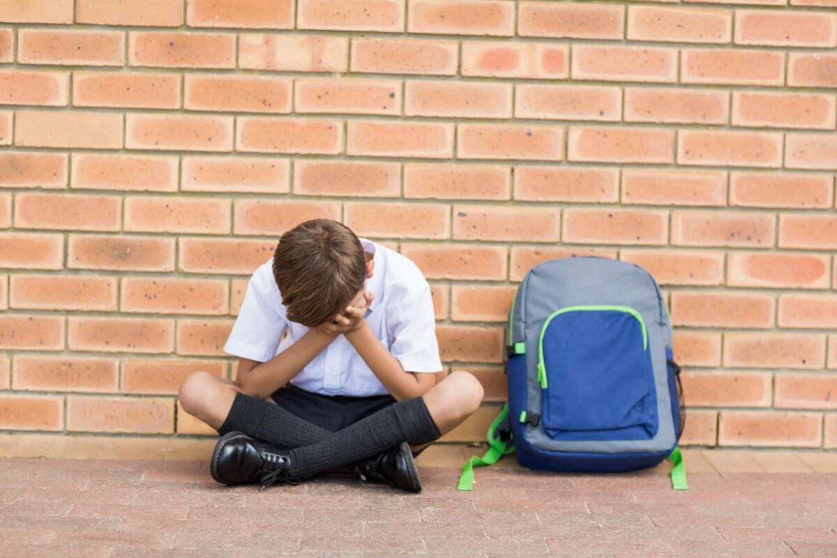 schoolboy with head in hands alone in a corridor