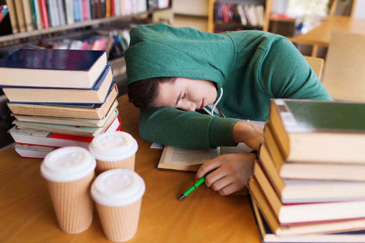 student asleep at desk with books and coffee cups