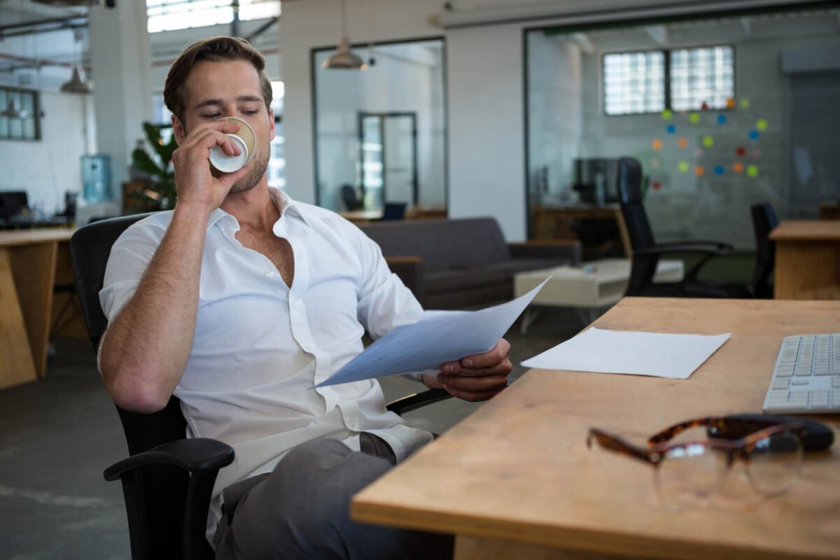 Businessman drinking coffee at a desk at work with shirt unbuttoned