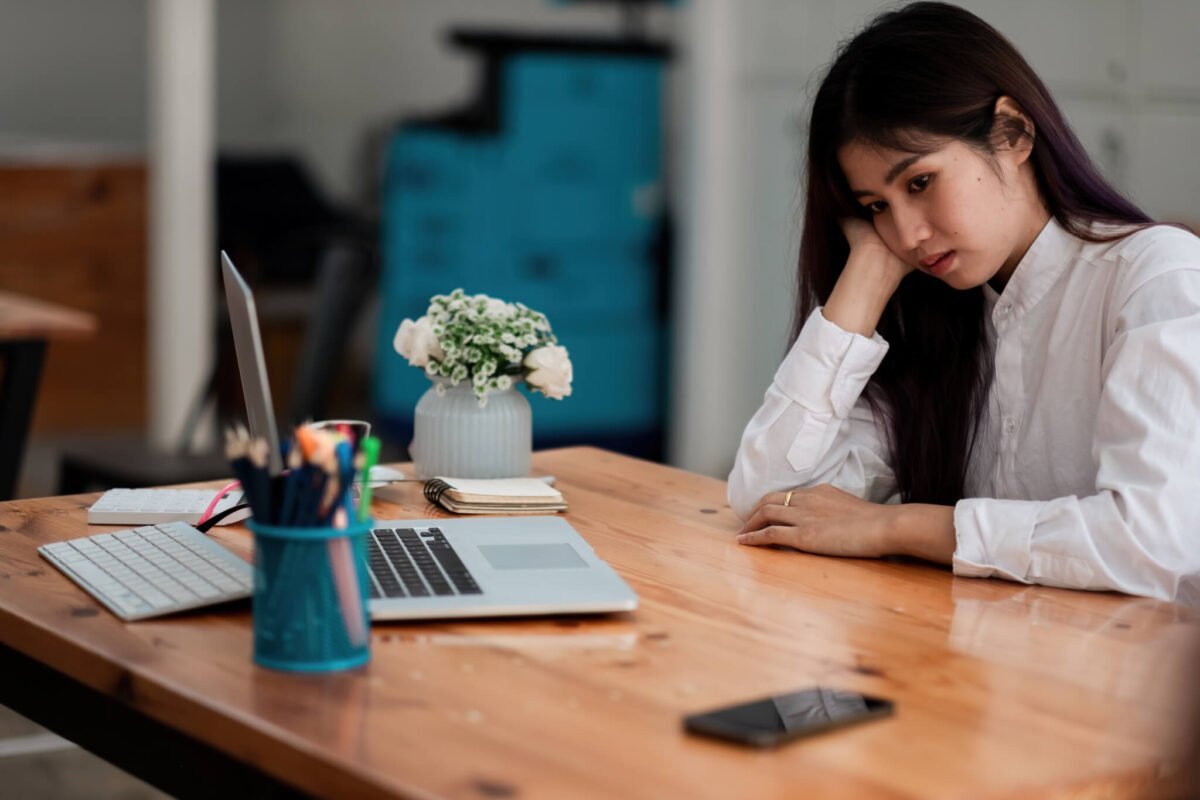 Asian woman at desk with head on hand looking bored and daydreaming