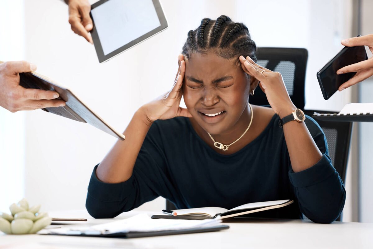 young woman with hands on head stressed surrounded by work tech stressed
