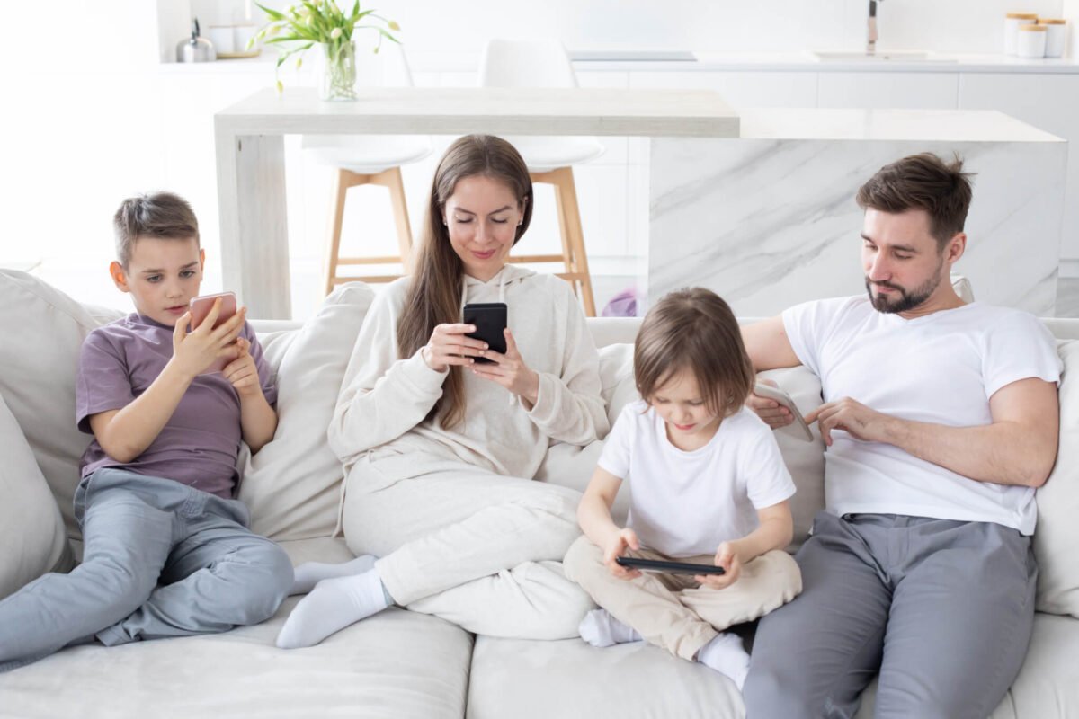 family of four sat in a very white open plan house all doomscrolling or playing games on mobile phones