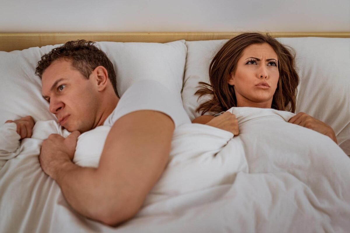 couple had argument in white bed and man is looking away from woman while woman is pouting