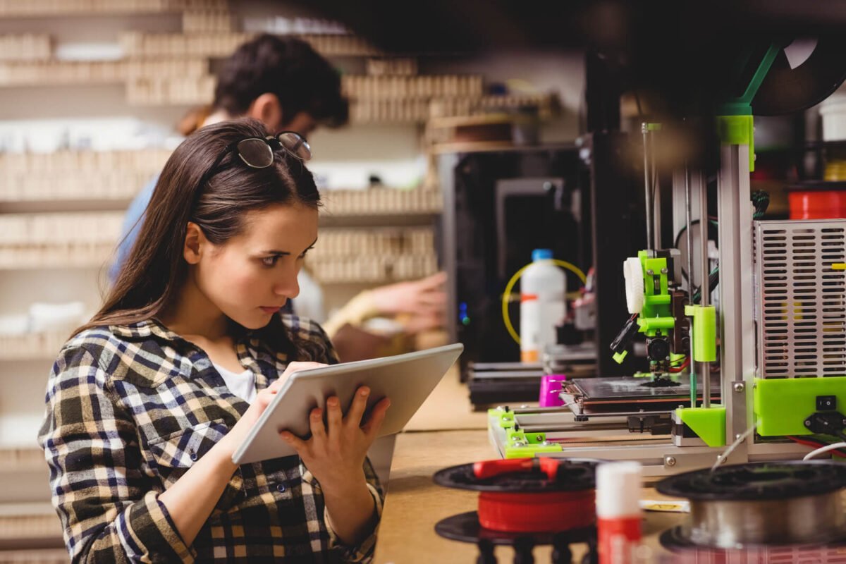 creative girl designer with notepad looking at 3d printer working