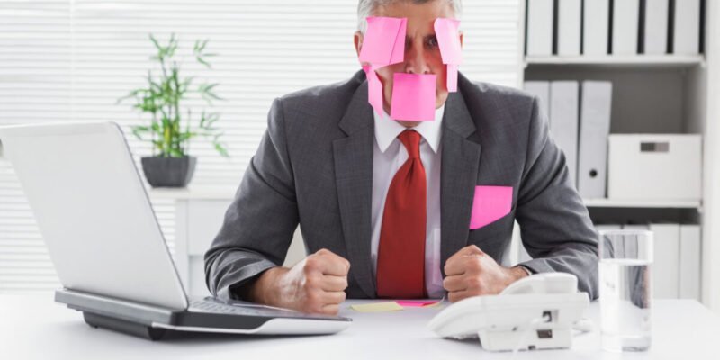 overwhelmed businessman with sticky notes on head in office
