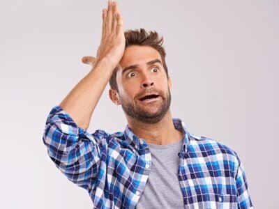 Duh. Studio shot of a young man looking forgetful against a gray background