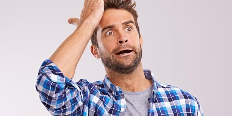 Duh. Studio shot of a young man looking forgetful against a gray background