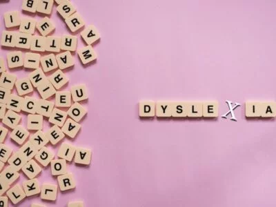 Alphabet letter tiles on pink background scrambled except for the word dyslexia
