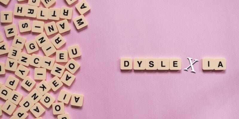 Alphabet letter tiles on pink background scrambled except for the word dyslexia