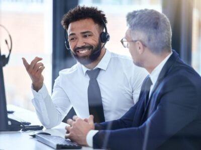 Call center agent or telemarketing employee consulting a business man and talking about company growth. Happy male customer service employee in training with an HR manager at the office