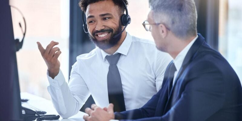 Call center agent or telemarketing employee consulting a business man and talking about company growth. Happy male customer service employee in training with an HR manager at the office