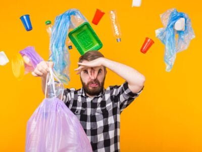 Man holding trash bag with plastic around him on an orange backgroundand environmental concept - man carrying garbage bag on yellow background