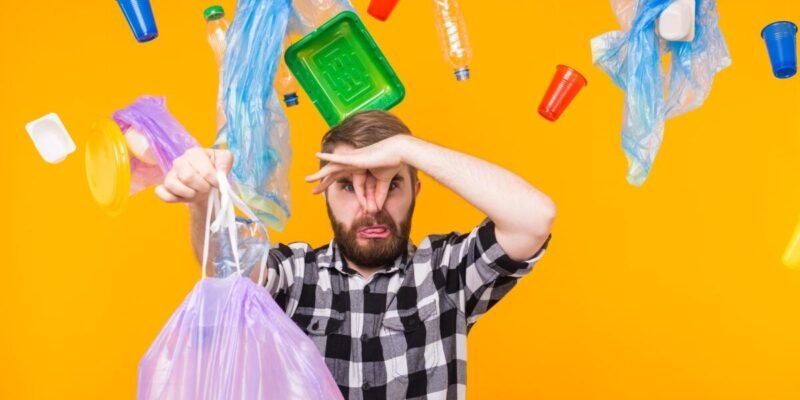 Man holding trash bag with plastic around him on an orange backgroundand environmental concept - man carrying garbage bag on yellow background