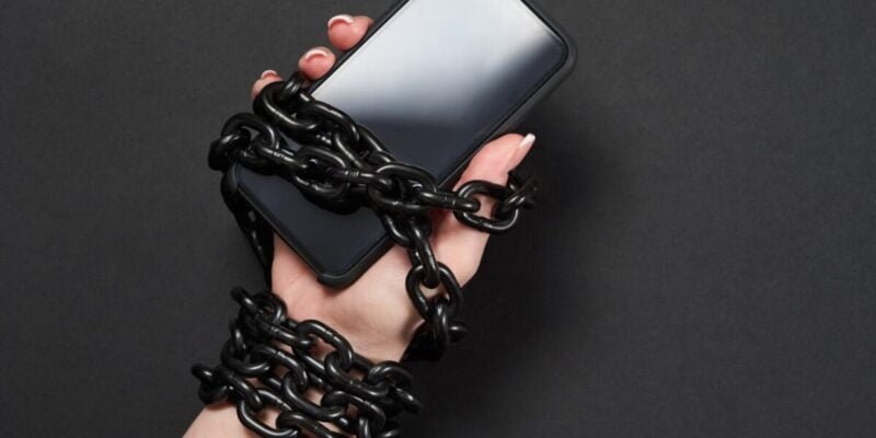 Close-Up Of Person Holding Mobile Phone And Chain to symbolize social media addiction