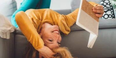 Blonde girl with ADHD reading a book while laying upside down on sofa