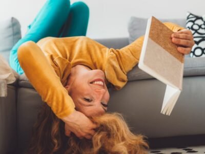 Blonde girl with ADHD reading a book while laying upside down on sofa