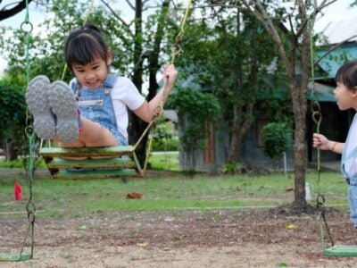 Cute little girl having fun in the outdoor playground. Young Asian sisters play together at school or kindergarten. Healthy summer activity for children.