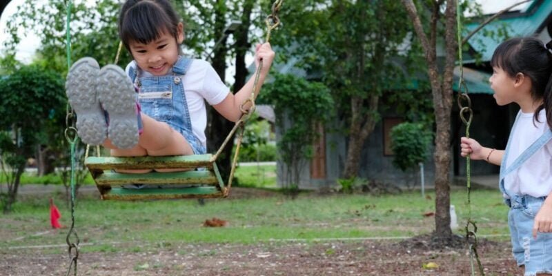 Cute little girl having fun in the outdoor playground. Young Asian sisters play together at school or kindergarten. Healthy summer activity for children.
