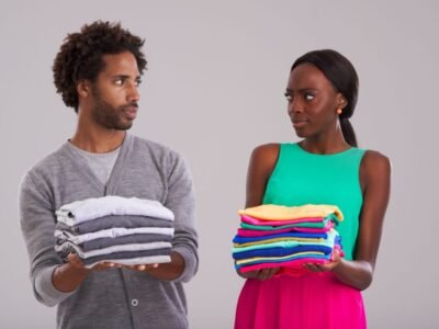 People, studio and pile of laundry in hand for neat, cleaning day or washing clothes together. Couple, surprise and shocked for organised wardrobe with color choice, fashion, perfectionism or ocd on grey background