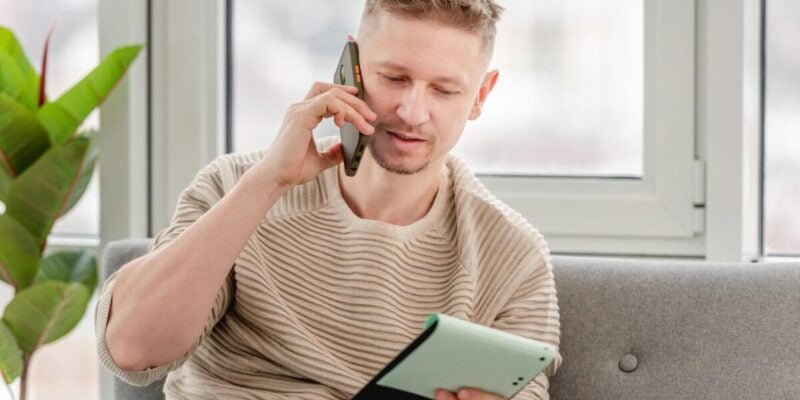 Autistic freelancer businessman talking by phone and holding notepad in his hands. Remote distance work at home during Covid pandemy