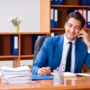 young man in blue suit working in an office smiling on phone