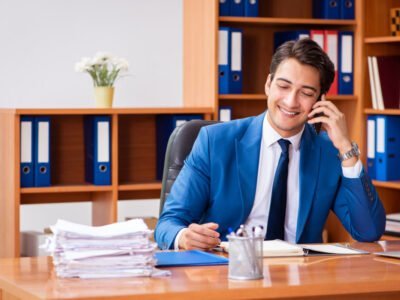 young man in blue suit working in an office smiling on phone