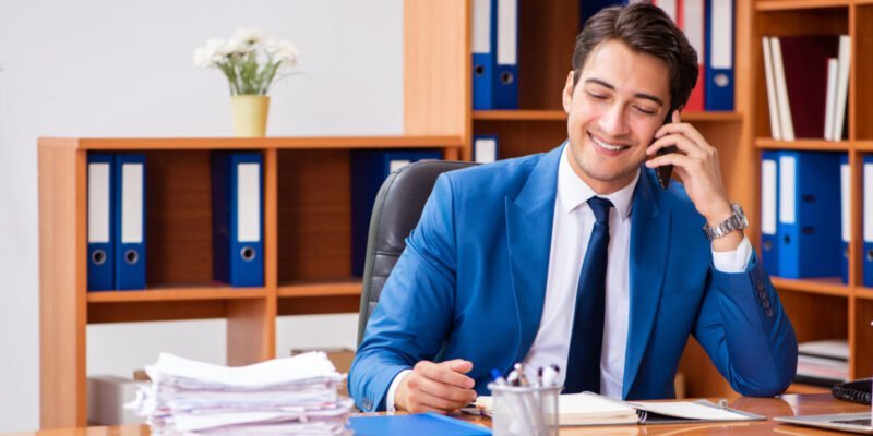 young man in blue suit working in an office smiling on phone