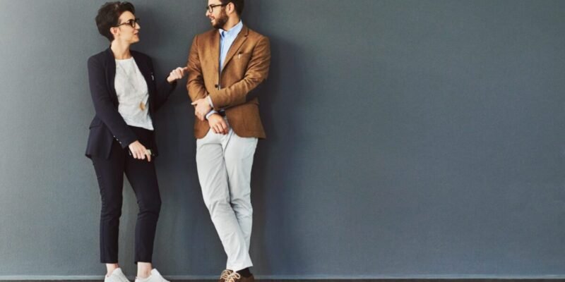 Shot of two designers having a conversation while leaning against a wall