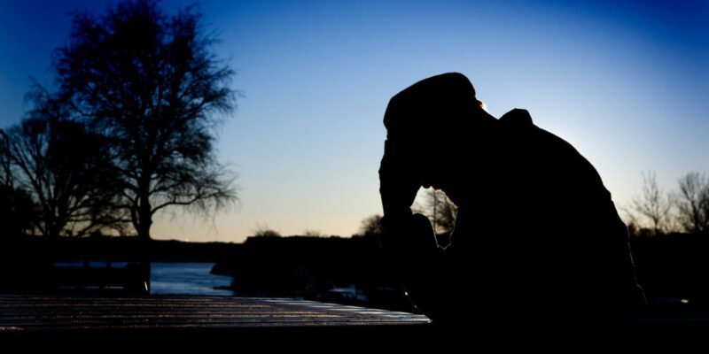 silhouette of man with head in hands outside during sunrise having a mid-life crisis