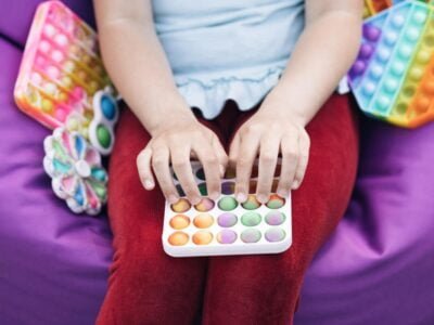 Young girl playing with Popit push pop bubble fidget toy. Topview of playing a popular anti-stress toy game. Children's hands play with the rainbow pop it fidget toy.