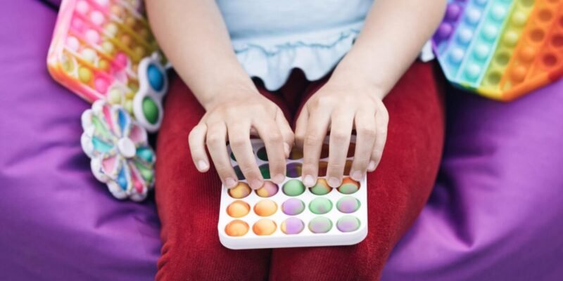 Young girl playing with Popit push pop bubble fidget toy. Topview of playing a popular anti-stress toy game. Children's hands play with the rainbow pop it fidget toy.