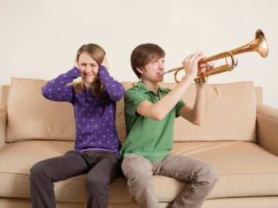 teenage boy and girl on sofa. boy is playing trumpet and girl has sensory processing disorder with hands over ears