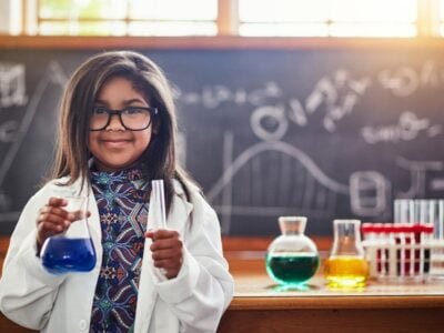 a cute little girl in a science lab smiling at camera in lab coat and her splinter skill is science