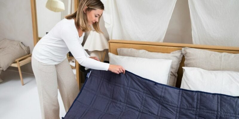 blonde woman with fibromyalgia putting a blue weighted blanket on the bed