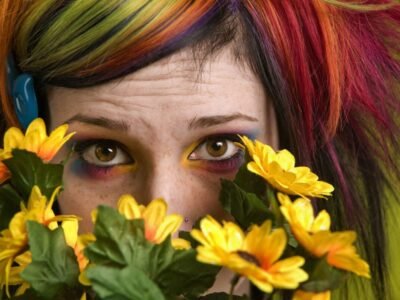 punk emo girl with red and green hair hiding behind yellow flowers