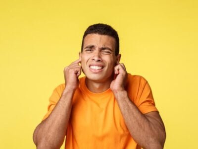 Turn off this annoying music, man hates noises Distressed and disturbed handsome guy, cringe and grimacing from bother, close ears, stooping, feel discomfort from loud noise