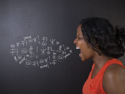 woman shouting next to chalkboard swearing with symbols on chalkboard in a cloud