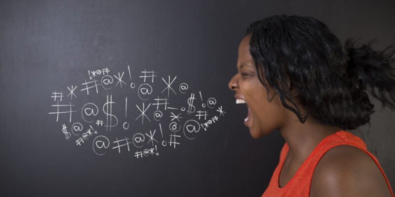 woman shouting next to chalkboard swearing with symbols on chalkboard in a cloud